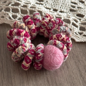 Close-up of a tricolor plush spiral hair tie with a soft felt ball on wood surface