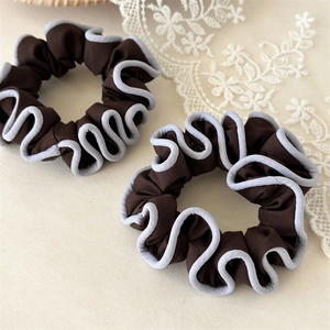 Detail of coffee brown fabric scrunchies with light blue wavy edges on a beige background