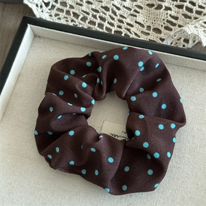Detail view of large brown satin scrunchie with blue polka dots on a textured plate