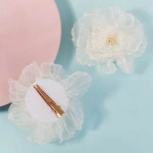 Détail de pinces à cheveux fleur en résille blanche avec pétales en organza et clip en métal doré