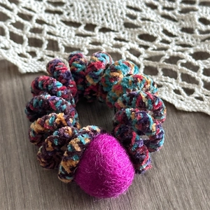 Detail shot of a spiral telephone cord hair tie with a soft magenta pom pom and knit texture