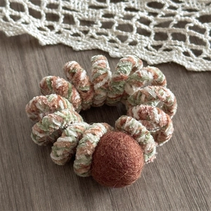 Detailed close-up of chenille spiral hair tie with brown pompom on wooden table