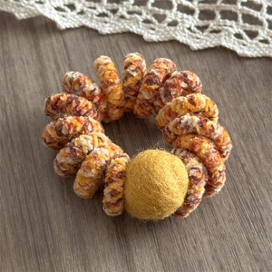 Detail view of winter spiral hair tie with orange velvet texture and yellow fuzzy pom-pom
