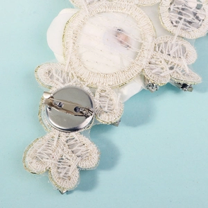 Detail of white 3D floral lace appliqué with gold trim and silver safety pin back