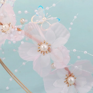 Close-up of pink fabric flowers with pearls and blue mesh butterflies on a golden headband