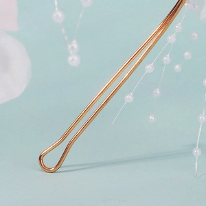 Detail of golden U-shaped hair pin with hanging white pearls on light blue background