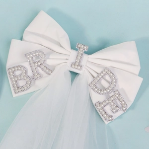 Detail of white bridal bow with pearl BRIDE lettering and double layer mesh veil
