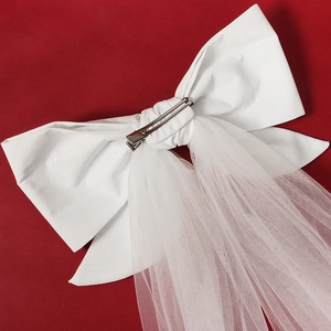Elegant white bridal bow hair clip with long tulle veil on a vibrant red background