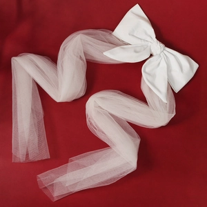 Elegant white satin bridal hair bow with long tulle veils on a vibrant red backdrop