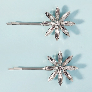 Detailed macro of two silver rhinestone flower hair clips on a light blue background