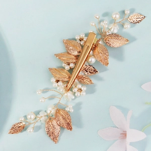 Golden bridal hair clip featuring delicate metal leaves and white pearls on blue background