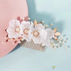 Bridal hair comb with white fabric flowers, pearls, and gold leaves on a pink background