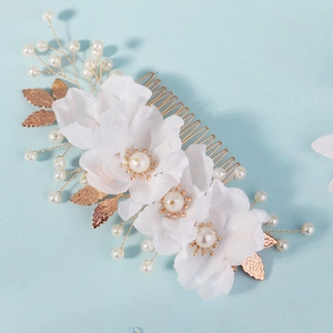 Close-up of bridal hair comb with white fabric flowers, pearls, and golden metal leaves