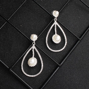 Detail of silver drop earrings featuring a hollow metal frame with white pearls and crystals