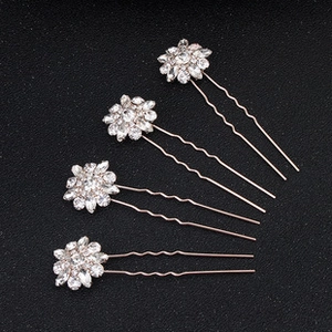 Dettaglio di quattro forcine floreali in oro rosa con strass su sfondo scuro testurizzato