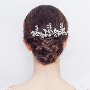 Détail d'une épingle à cheveux de mariée aux feuilles argentées sur un chignon tressé