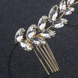 Macro view of gold olive branch bridal hair comb with marquise crystals on black background