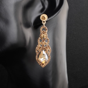Macro shot of gold alloy bridal drop earrings with amber crystals on a black model ear