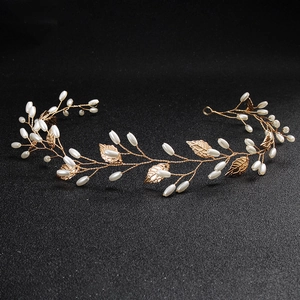 Close-up of handmade bridal headband with gold leaves and white drop pearls on dark background
