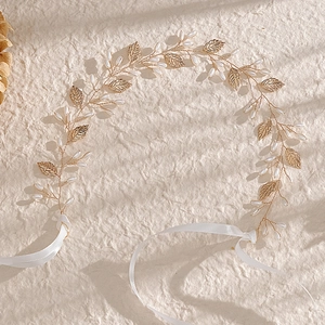 Handmade bridal hair vine with gold leaves and white pearls on elegant textured background