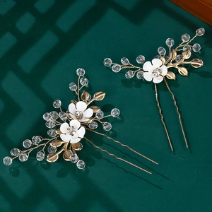 Elegant gold bridal hair pins with white flowers, crystals, and leaf details on green backdrop