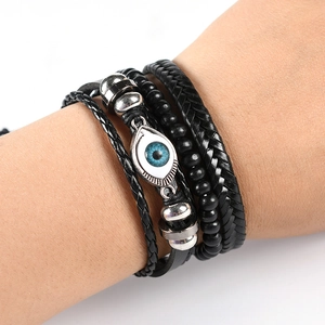 Close-up of black layered leather bracelets featuring an evil eye charm and metal beads
