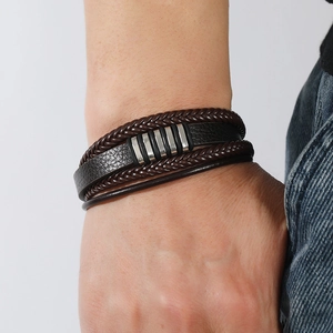 Gros plan d'un bracelet multicouche en cuir tressé pour homme avec breloques métalliques