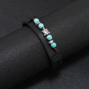 Dettaglio di un bracciale multistrato in pelle con perle turchesi e ciondolo a tartaruga argento