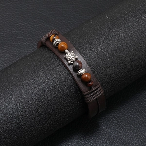 Dettaglio di un bracciale in pelle vintage con perle occhio di tigre e ciondolo a tartaruga