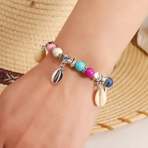 Close-up of bohemian colorful beaded bracelet with seashell charms on a beach hat