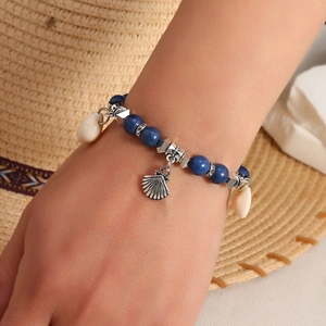 Detail of bohemian beach bracelet with blue beads, silver scallop charm and white sea shells