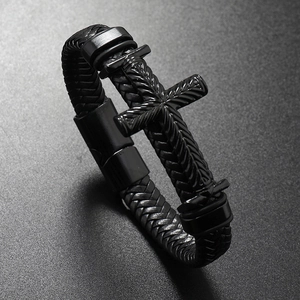 Detailed macro view of woven black leather bracelet with a textured metal cross charm