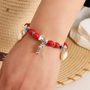 Detail of bohemian red beaded bracelet featuring a silver fishbone and white shell charm