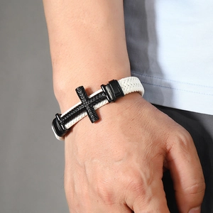 Close-up of white braided leather bracelet with textured black metal cross charm on wrist