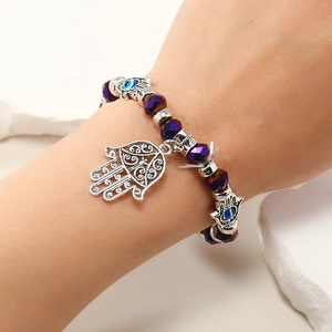 Detalle de pulsera de cuentas púrpuras con mano de Fátima y amuleto Evil Eye en la muñeca