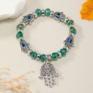Detalle de Mano de Fátima y Ojo Turco en pulsera de cristal verde con decoración otoñal