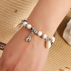 Detail of bohemian seashell charm bracelet with white marble beads on a vacation background