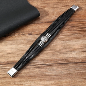 Detail of multi-layer black leather bracelet featuring a silver compass charm and magnetic clasp