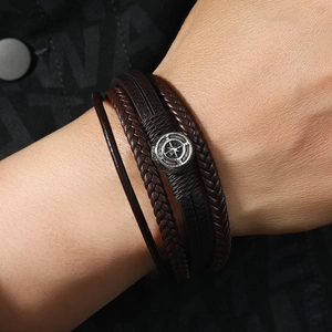 Close-up of a multi-layer brown braided leather bracelet with silver compass charm for men