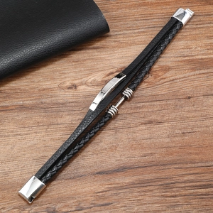 Detail of multi-layer black braided leather bracelet with silver metal plates on wood