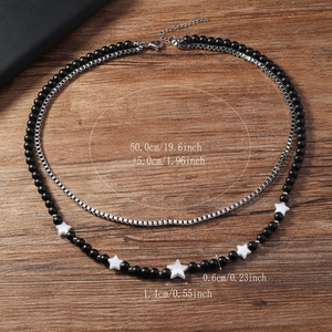 Détail du collier double couche avec perles noires, étoiles et chaîne à maillons carrés
