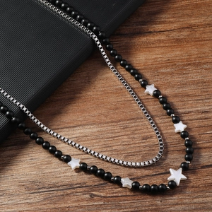 Détail du collier double couche avec perles mates noires, étoiles blanches et chaîne box