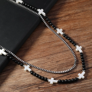 Détail d'un collier double épaisseur pour homme avec perles noires et croix blanche