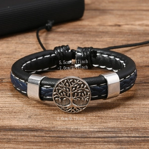 Detail of hand-woven leather bracelet featuring metal Tree of Life charm on wood