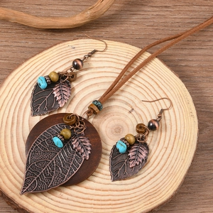 Vintage style handmade jewelry set with leaf charms and wooden discs on a rustic stump