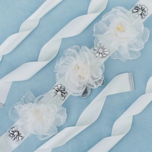 Macro view of handmade organza flowers and crystals on a white bridal sash