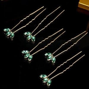 Detailed view of five gold-plated bridal hair pins with emerald green marquise crystals