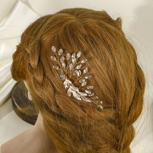 Detailaufnahme eines roségoldenen Braut-Haarkamms mit Kristallen in braunem lockigem Haar