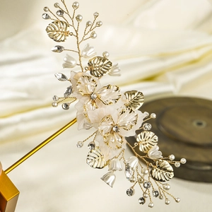 Detail showing handmade bridal hair clip with gold metal leaves and ivory petals
