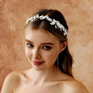 Close-up of golden leaf and white flower headband worn by a smiling model